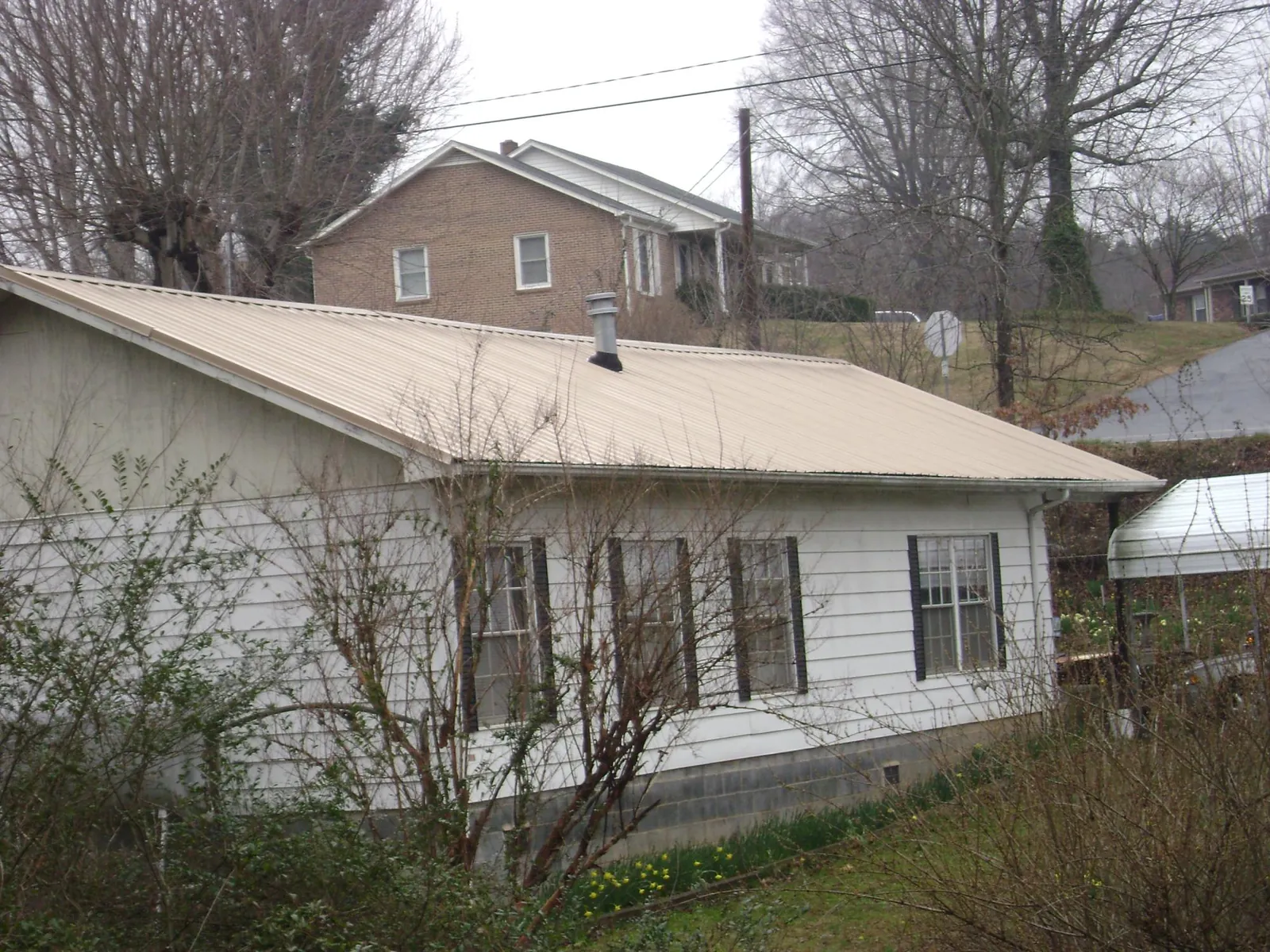 Tan metal roof on a white sided house set into a hillside — Commercial Roofing by Roofing Brothers in Lithia Springs
